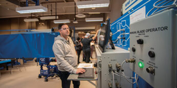 Student operates a computer at a control panel labeled 