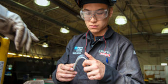 Student with welding mask flipped up looks over a piece of metal