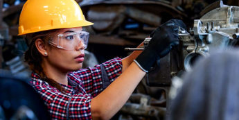 Student wearing a hardhat and safety glasses works on a machine