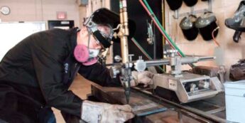 Student operates a machine in a workshop setting.