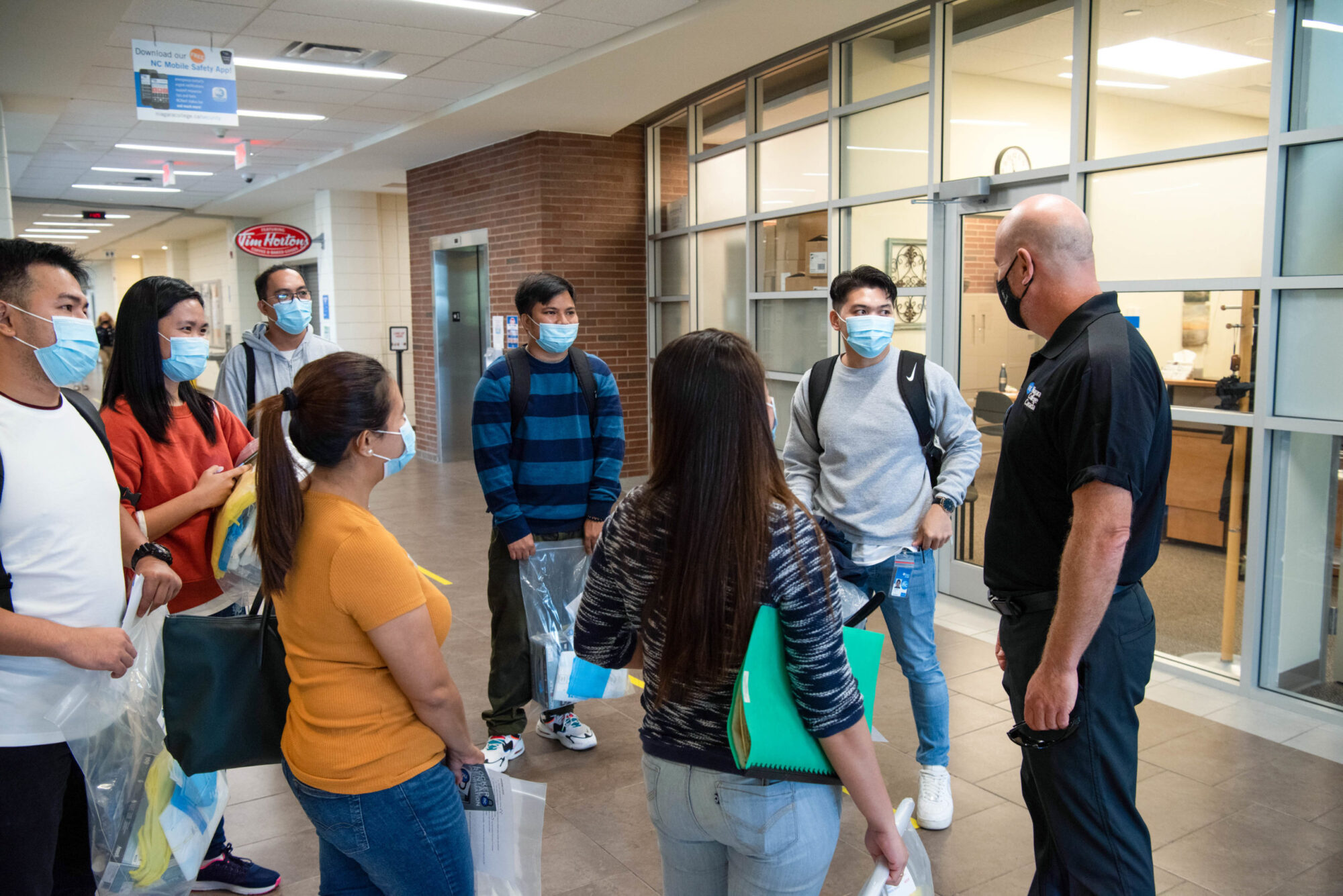 A man speaks with a group of students inside at the Welland Campus.