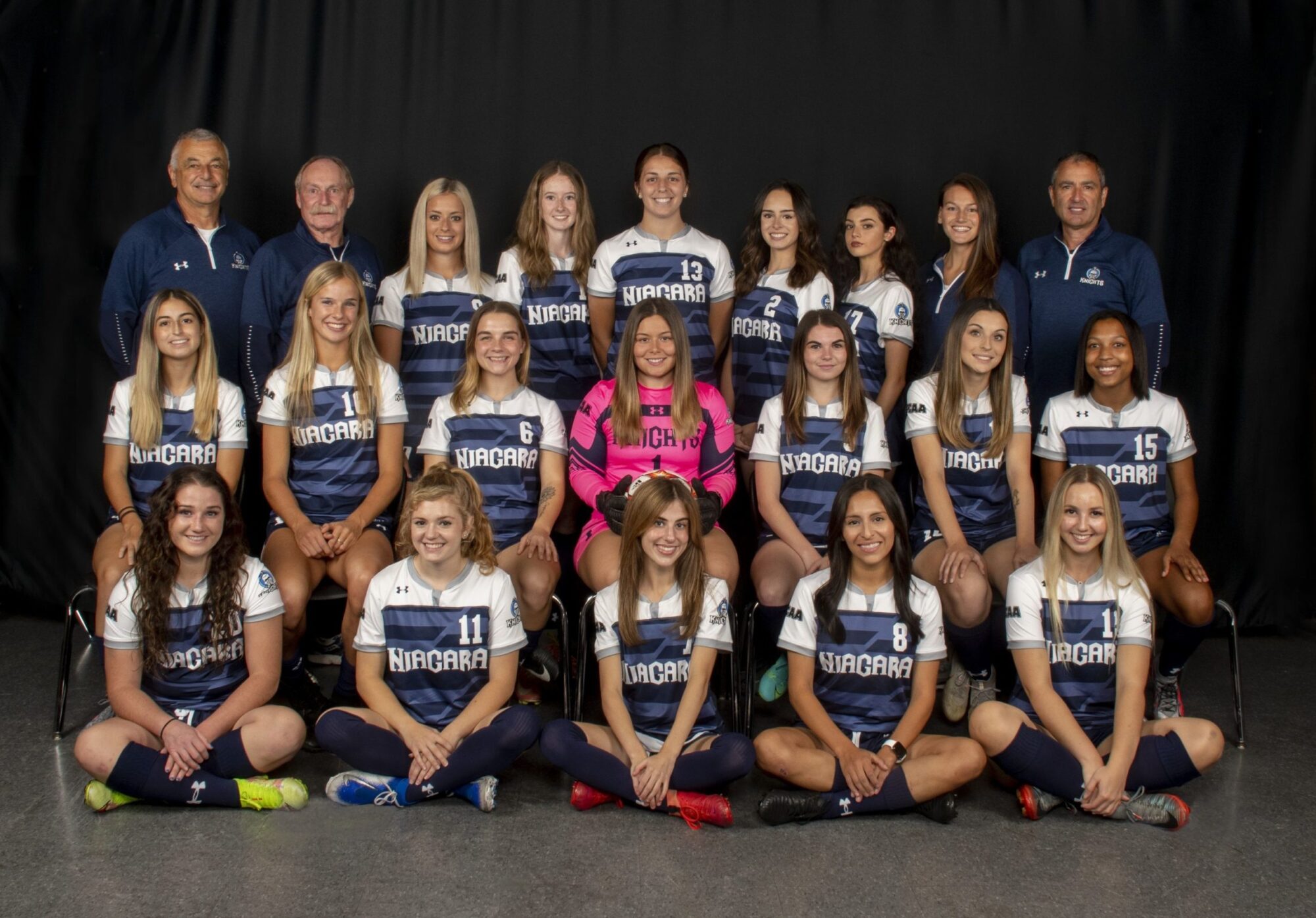 female soccer players wearing their jerseys smile at the camera for a team photo along with coaching staff team