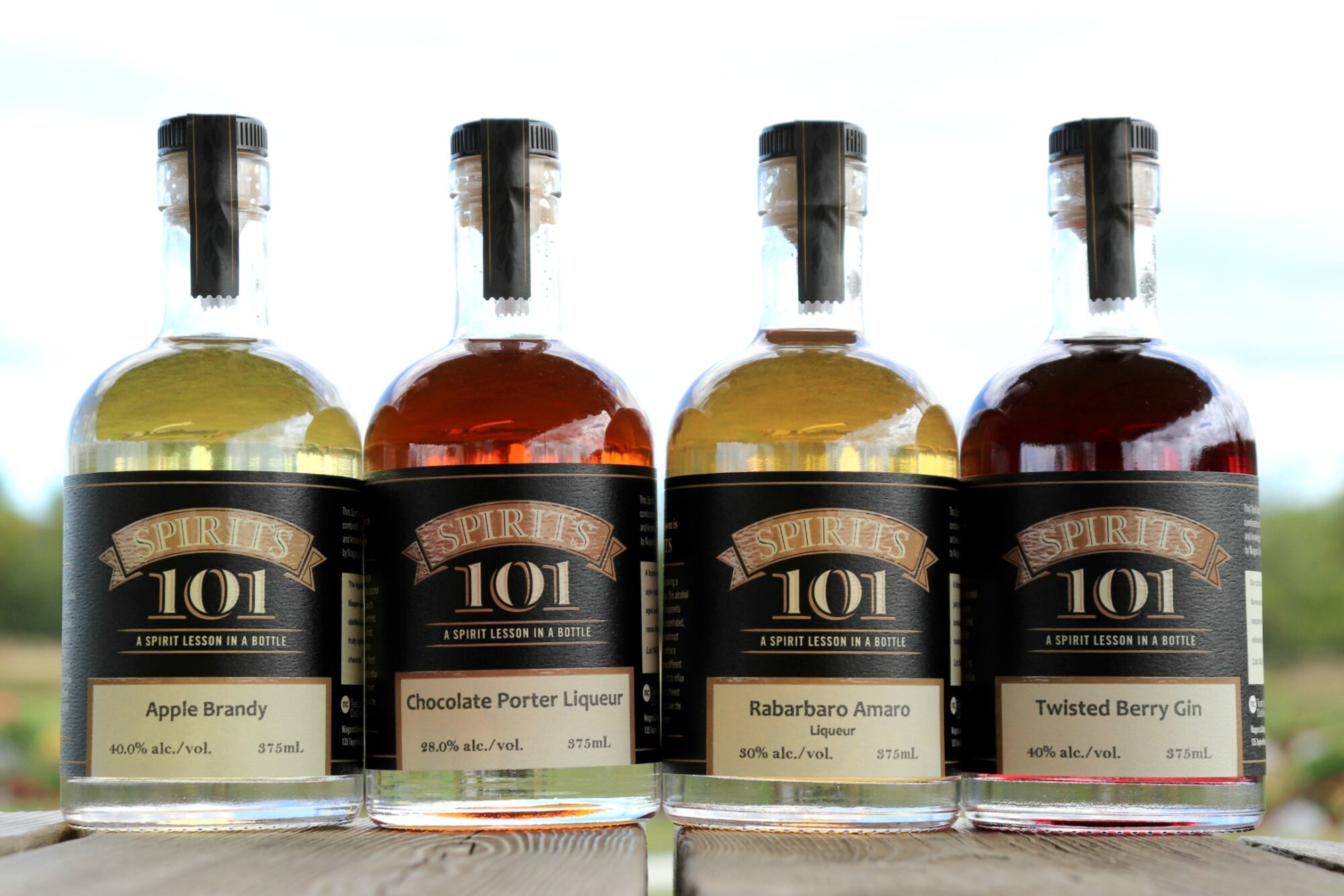 four bottles of spirits lined up in a row against an outdoor backdrop