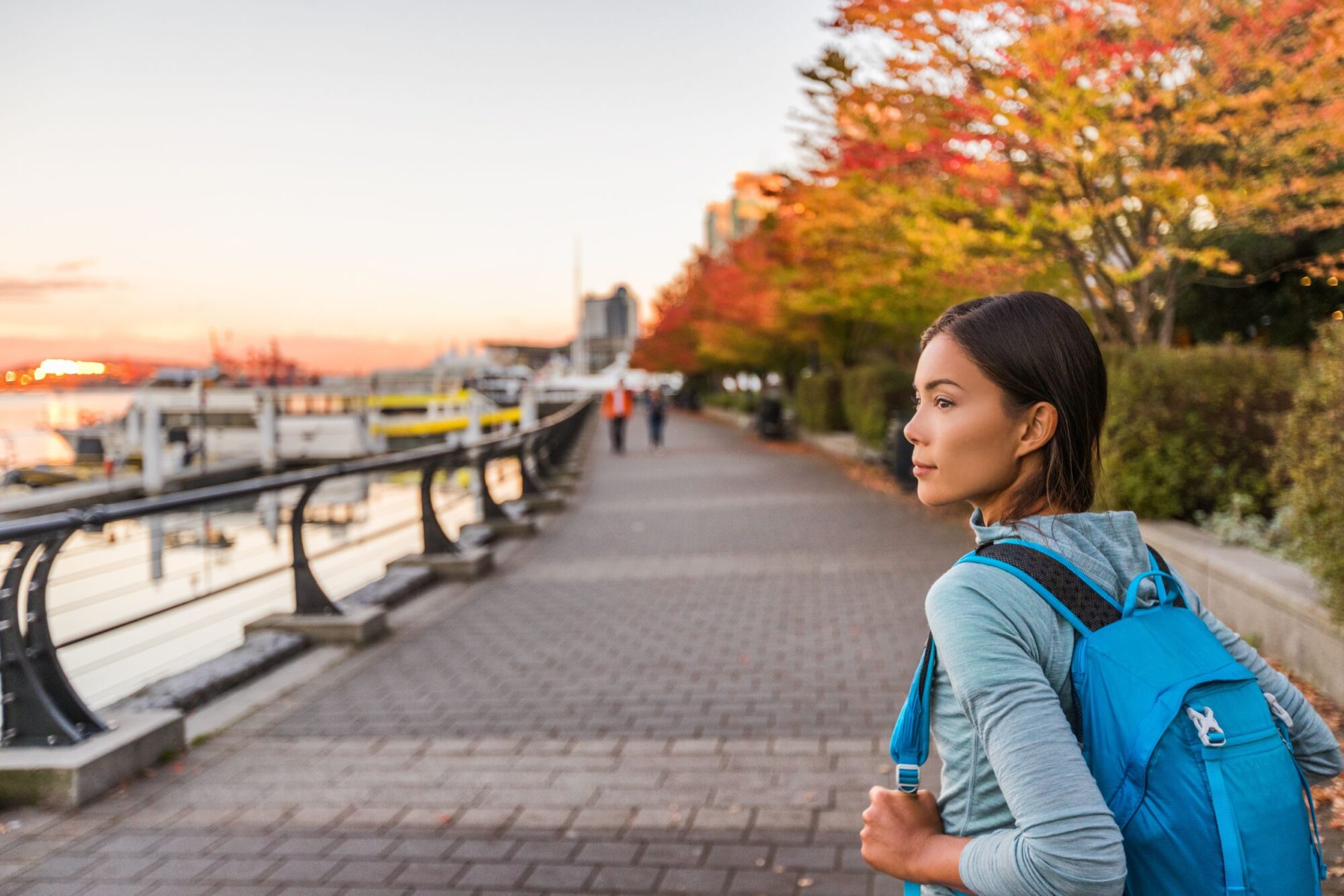 a female traveler wearing a blue backpack looks off to the side while walking on a path in the fall
