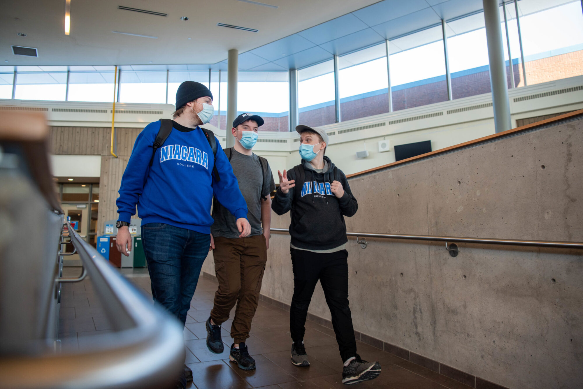 Three students walk together and converseon campus wearing masks.