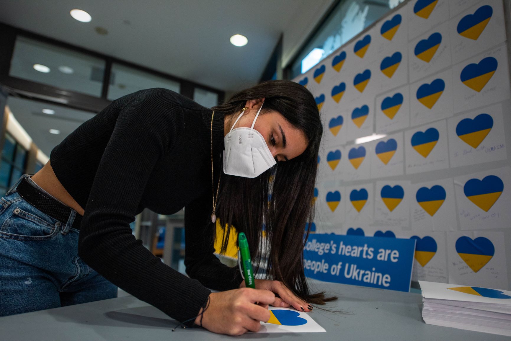 a student writes a message on a note card displaying a blue and yellow heart
