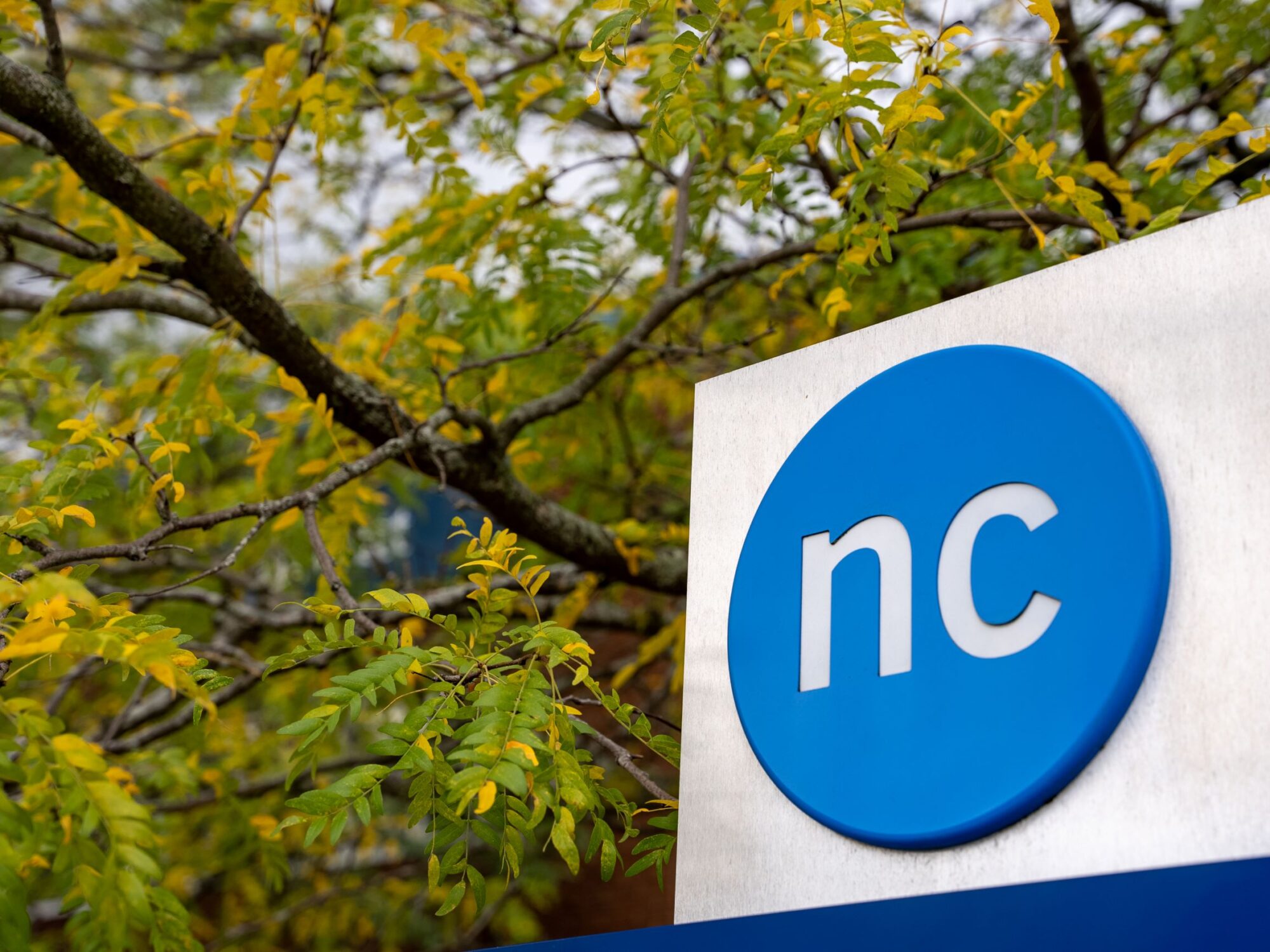 The NC button logo on an outdoor sign with fall foliage in the background