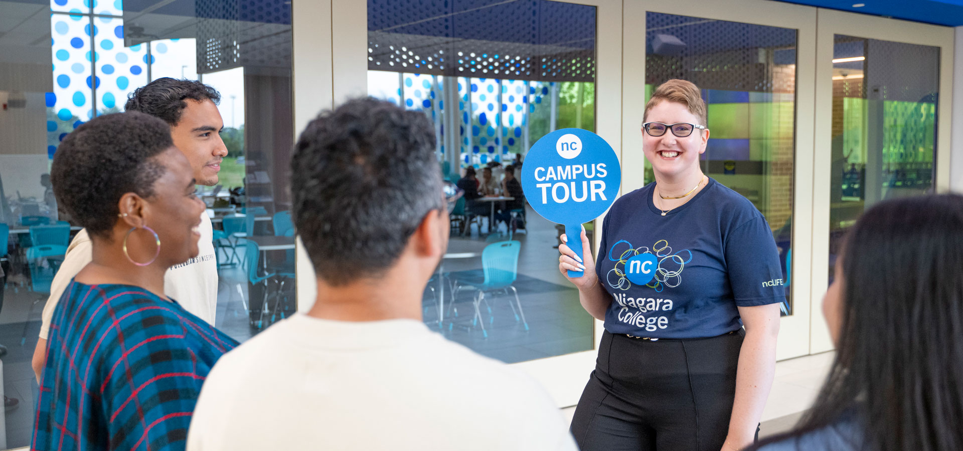 NC campus tour guide holding a Campus Tour sign guides a group of visitors through the Welland campus