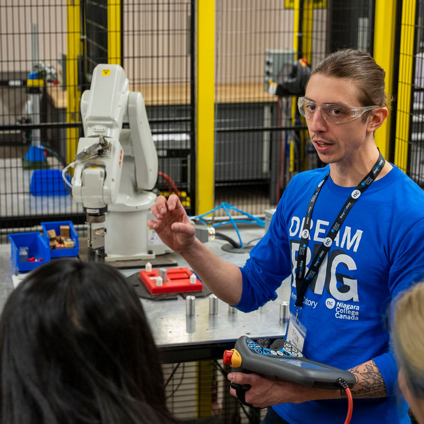 NC student wearing NC t-shirt and lanyard demonstrates mechanical equipment to a group