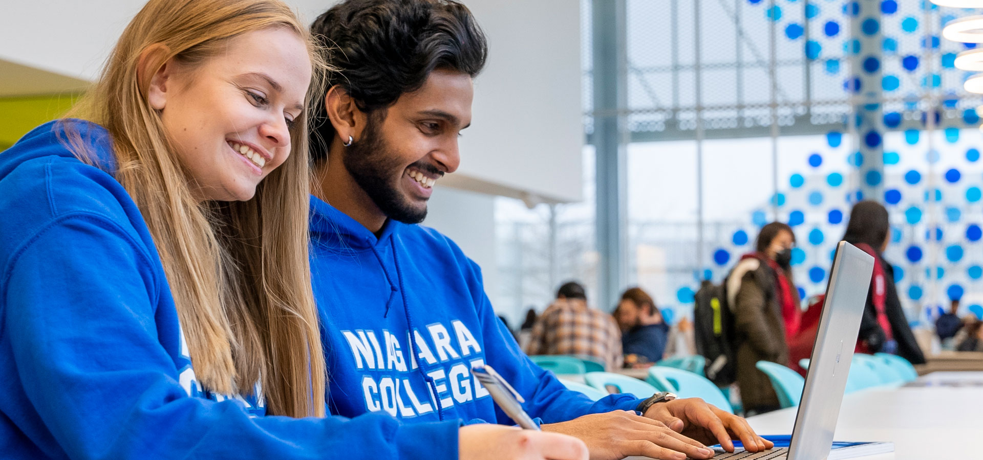 Two students wearing NC hoodies work together on laptops