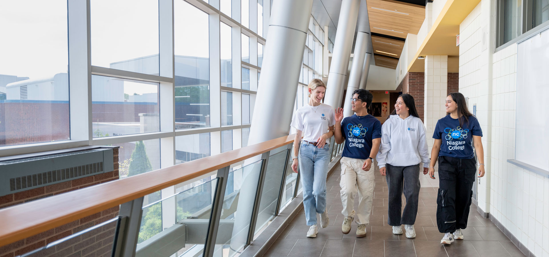 Four students in NC t-shirts walking in a brightly lit hallway