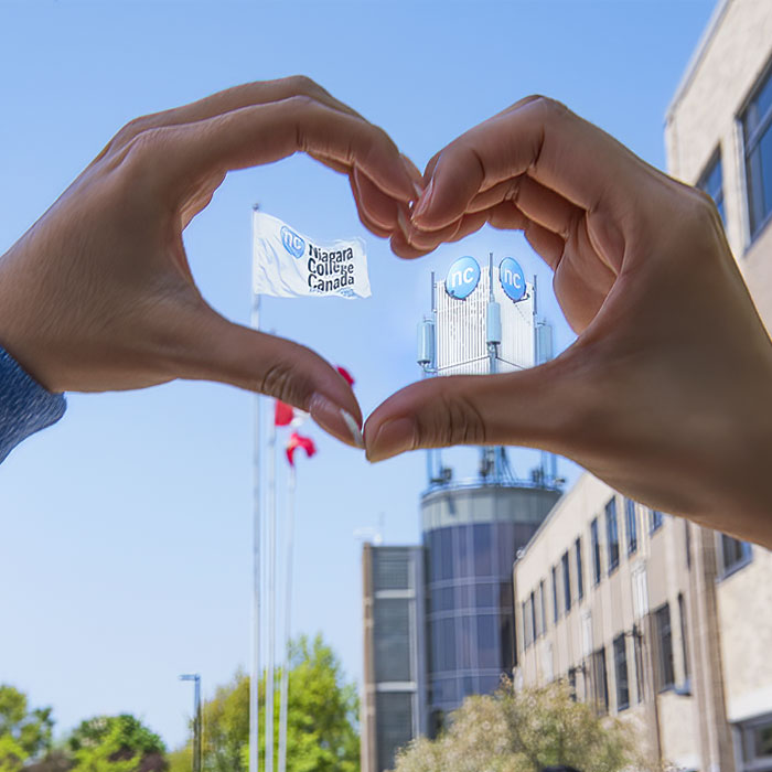 Hand forming the shape of a heart around a view of NC flagpole and tower