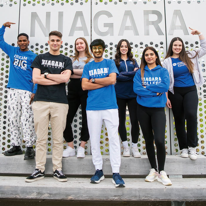 Group of students wearing NC clothing pointing at Niagara sign