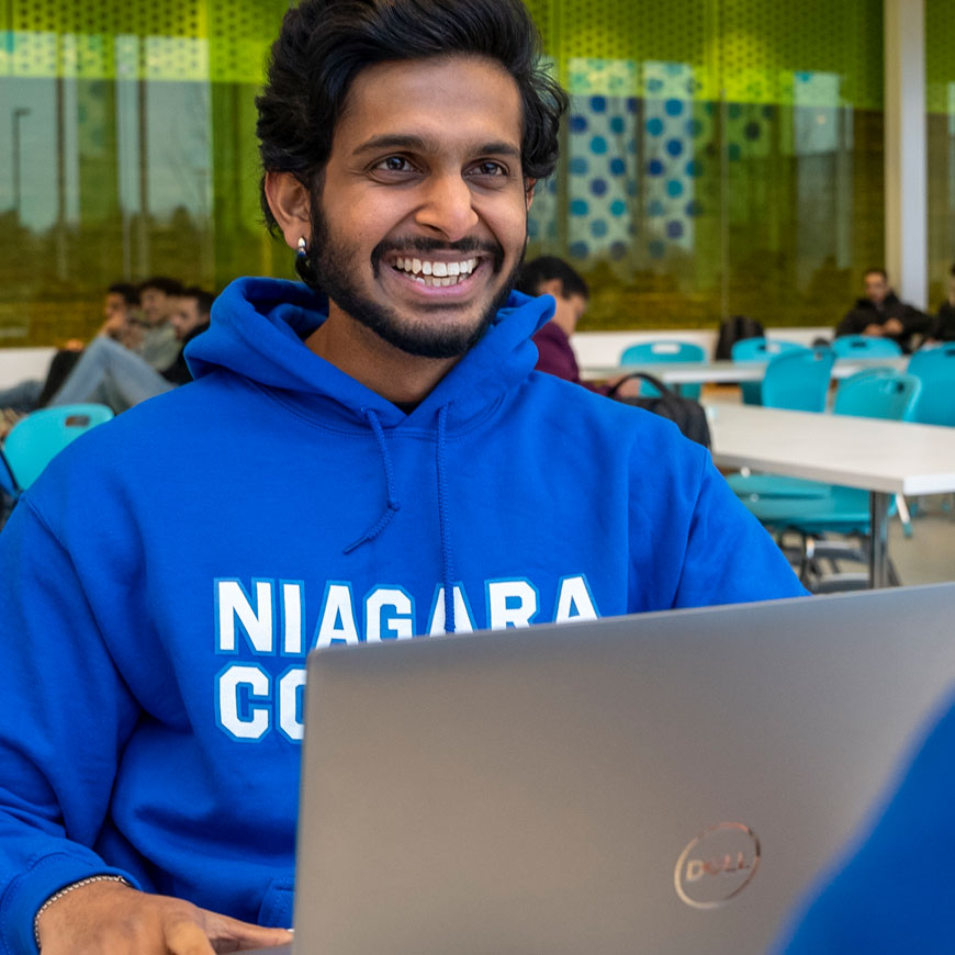 Student in NC hoodie works on a laptop in the cafeteria