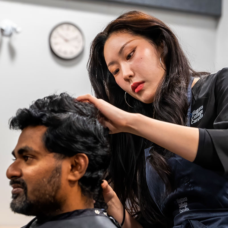 Female student concentrates on cutting the hair of a client