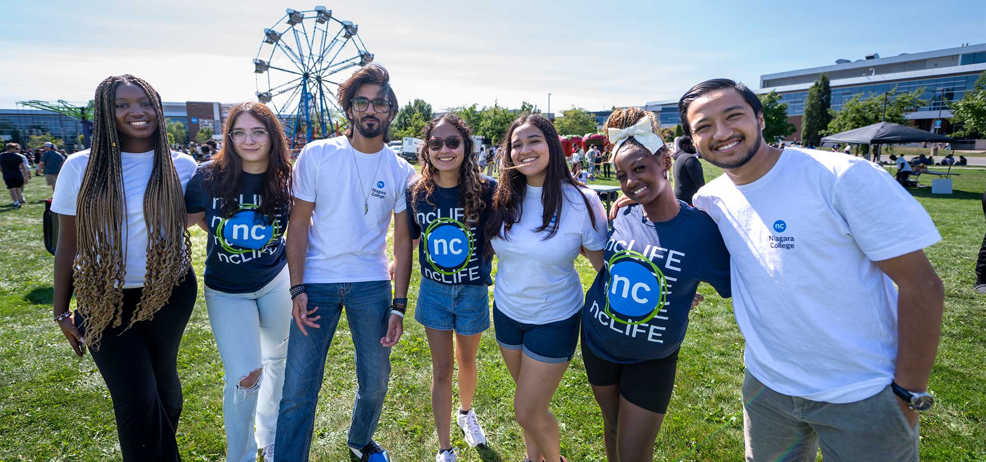 Students wearing NC T-shirts pose together outdoors on a sunny day