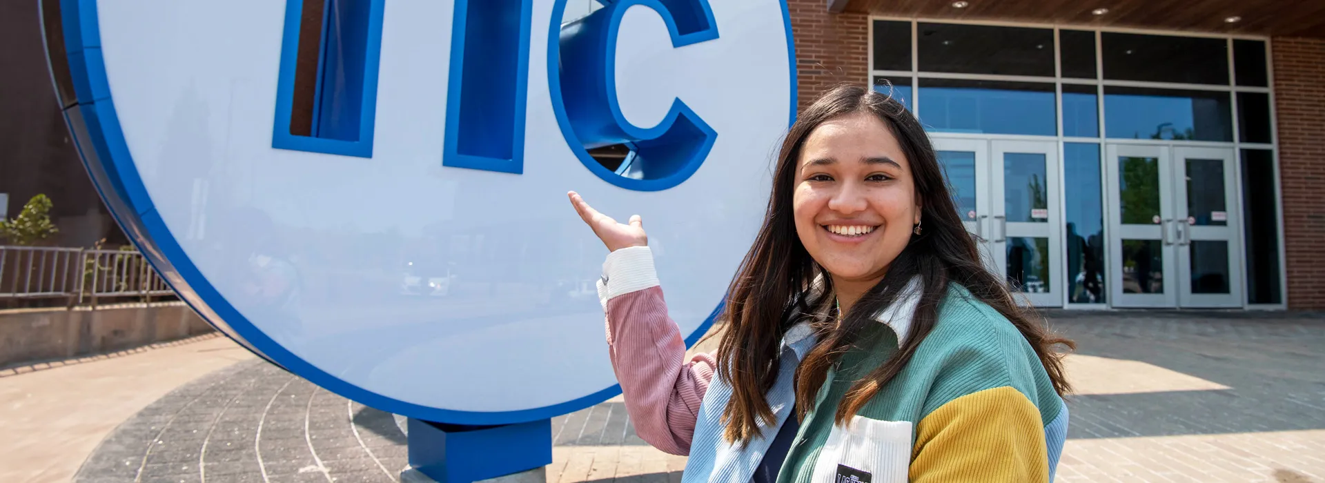 Student posing in front of and pointing at large NC button statue