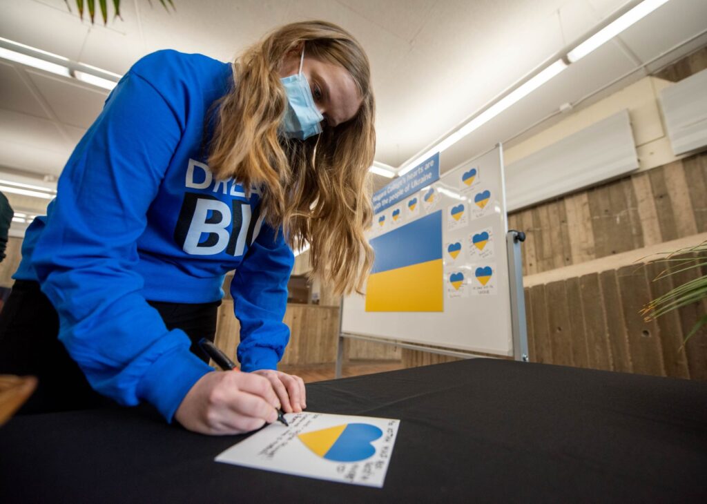 a student writes a message on a note card displaying a blue and yellow heart