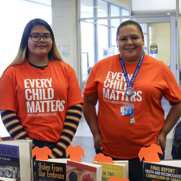 Two students wearing Every Child Matters t-shirts at a booth